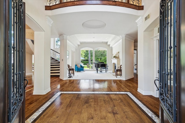 entryway featuring hardwood / wood-style flooring, visible vents, a towering ceiling, ornate columns, and stairs