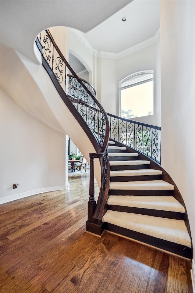 staircase featuring baseboards, wood finished floors, a high ceiling, crown molding, and recessed lighting