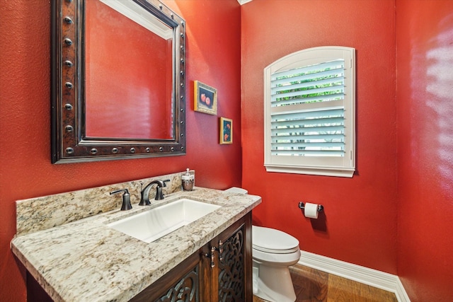 half bathroom featuring wood finished floors, vanity, toilet, and baseboards