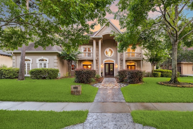 view of front of property featuring french doors, a front yard, a balcony, and stucco siding