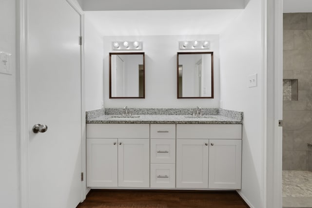 bathroom featuring double vanity, wood finished floors, a tile shower, and a sink