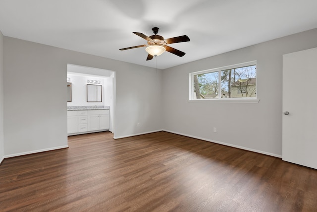 unfurnished bedroom featuring baseboards, ensuite bath, wood finished floors, and a ceiling fan