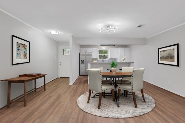 dining room featuring visible vents, baseboards, wood finished floors, and crown molding