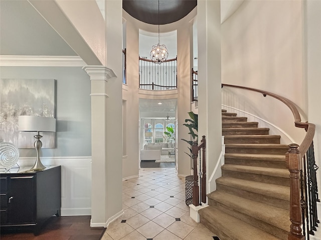 entryway featuring stairway, a wainscoted wall, decorative columns, a high ceiling, and an inviting chandelier