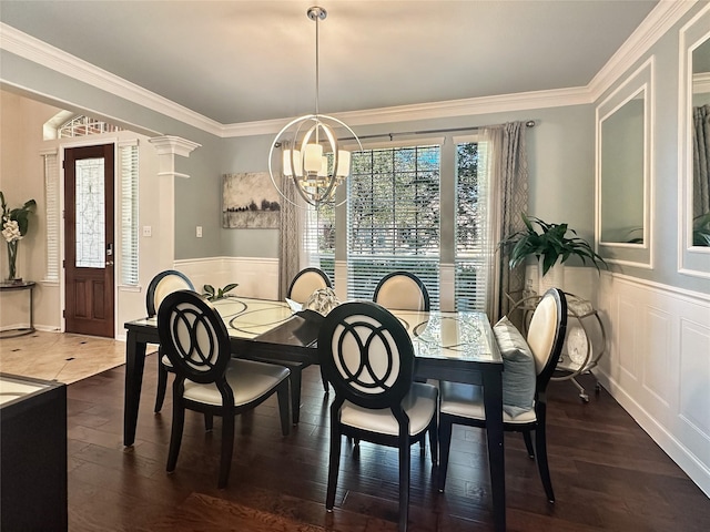 dining area with wood finished floors, wainscoting, a decorative wall, crown molding, and a chandelier