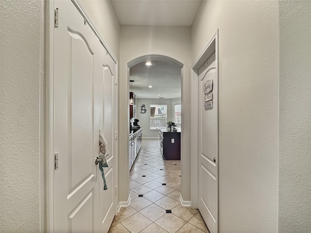 hallway featuring light tile patterned flooring, baseboards, and arched walkways