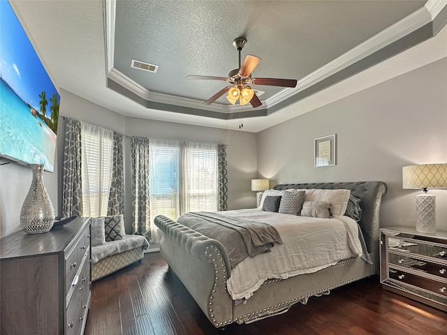 bedroom with visible vents, crown molding, dark wood finished floors, a tray ceiling, and a textured ceiling