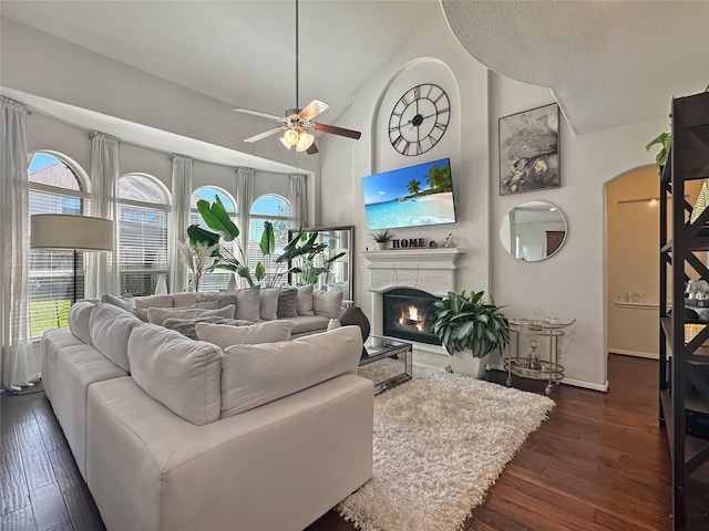 living room with dark wood-type flooring, high vaulted ceiling, a glass covered fireplace, baseboards, and ceiling fan