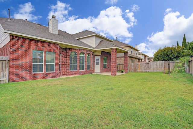 back of house with a yard, a fenced backyard, a chimney, a patio area, and brick siding