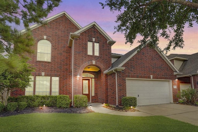 traditional-style house with a yard, driveway, brick siding, and an attached garage