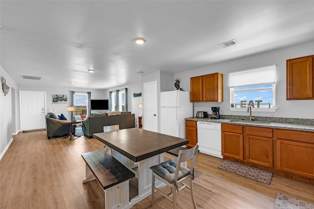 kitchen with white appliances, brown cabinetry, visible vents, and a sink