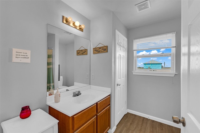 bathroom with vanity, wood finished floors, visible vents, baseboards, and toilet