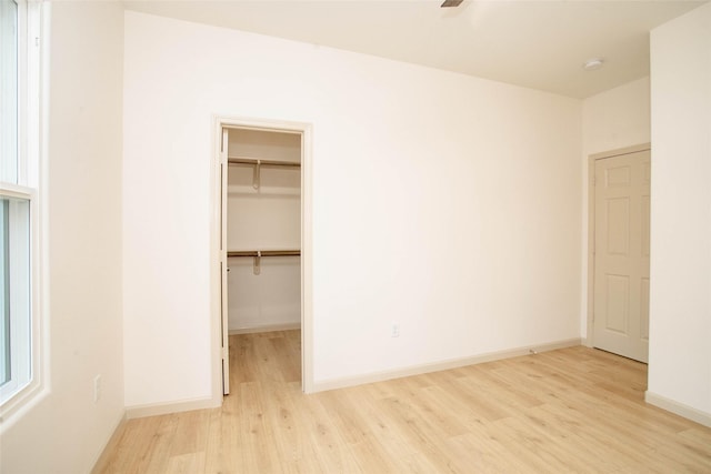 unfurnished bedroom featuring a closet, a spacious closet, baseboards, and wood finished floors