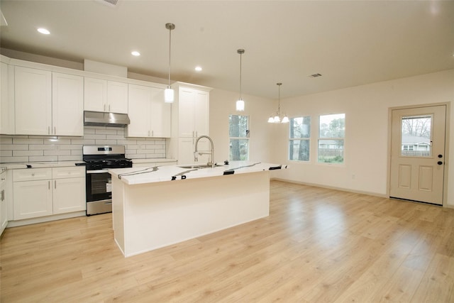 kitchen featuring under cabinet range hood, a sink, stainless steel range with gas cooktop, decorative backsplash, and light wood finished floors