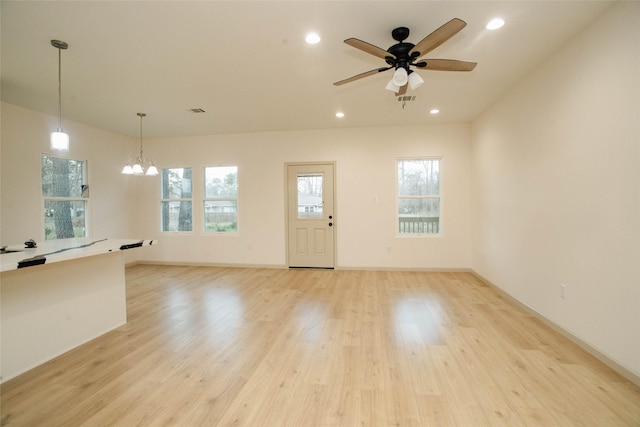 unfurnished living room featuring light wood-style flooring, ceiling fan with notable chandelier, a wealth of natural light, and recessed lighting