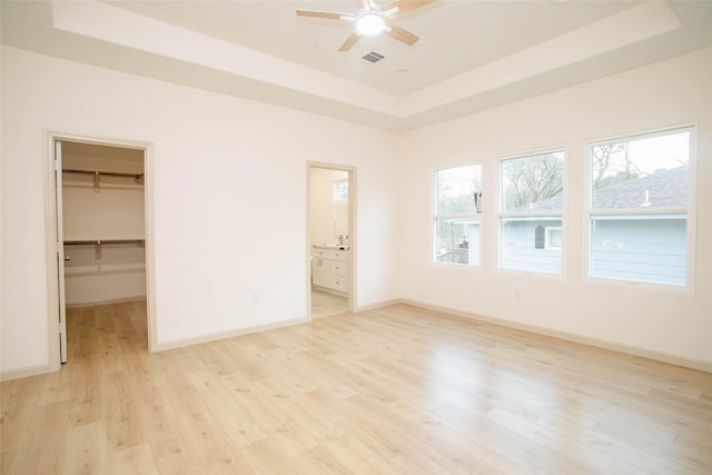 unfurnished bedroom with baseboards, a tray ceiling, and light wood-style floors