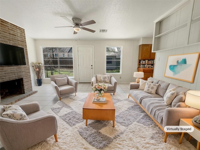 living area with visible vents, a brick fireplace, ceiling fan, light tile patterned flooring, and a textured ceiling