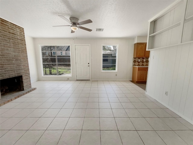 unfurnished living room with visible vents, a textured ceiling, a fireplace, light tile patterned floors, and ceiling fan