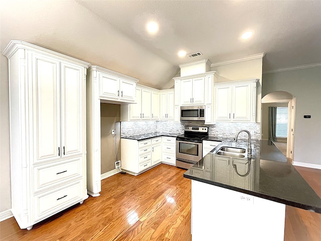 kitchen with arched walkways, decorative backsplash, appliances with stainless steel finishes, a peninsula, and a sink