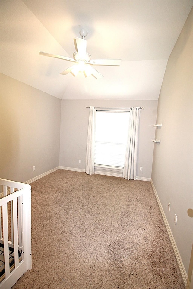 carpeted empty room with a ceiling fan, lofted ceiling, and baseboards