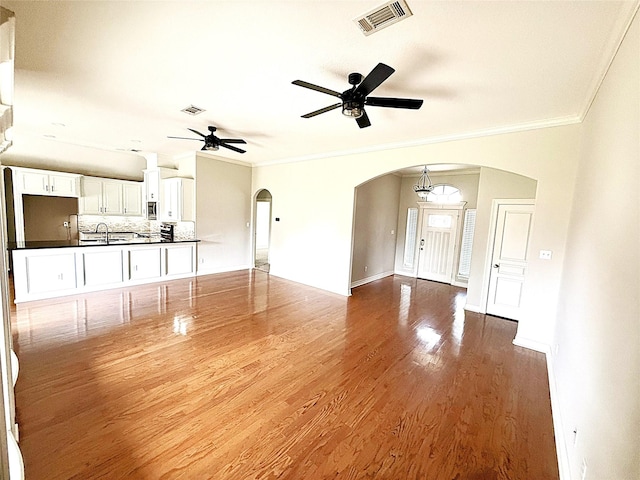 unfurnished living room featuring arched walkways, visible vents, ornamental molding, and ceiling fan