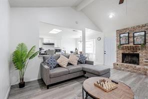 living area with high vaulted ceiling, a brick fireplace, beam ceiling, and wood finished floors