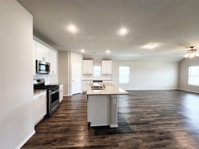 kitchen featuring light stone counters, dark wood finished floors, a center island with sink, appliances with stainless steel finishes, and a sink