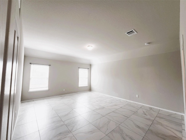 spare room with marble finish floor, visible vents, and baseboards