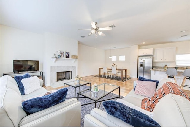 living room featuring visible vents, baseboards, light wood-type flooring, a premium fireplace, and a ceiling fan