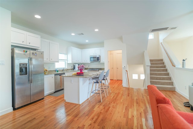 kitchen featuring a kitchen island, a breakfast bar, light wood-type flooring, stainless steel appliances, and white cabinetry