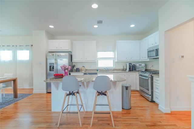 kitchen with a breakfast bar area, visible vents, stainless steel appliances, white cabinets, and a center island