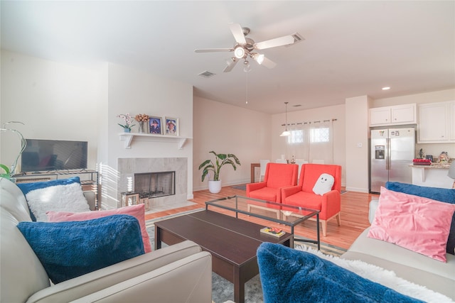 living room featuring visible vents, a ceiling fan, a tiled fireplace, light wood finished floors, and baseboards