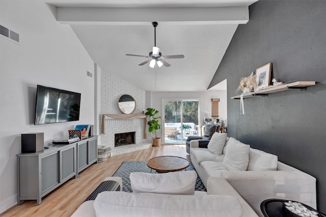 living room featuring light wood-type flooring, visible vents, beam ceiling, a fireplace, and ceiling fan