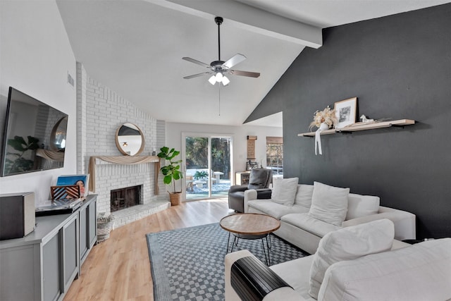 living room featuring light wood finished floors, ceiling fan, beam ceiling, a fireplace, and high vaulted ceiling