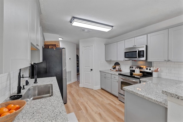 kitchen featuring visible vents, backsplash, light wood-type flooring, appliances with stainless steel finishes, and a sink