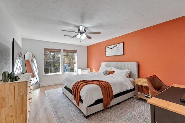 bedroom featuring visible vents, baseboards, ceiling fan, light wood-type flooring, and a textured ceiling