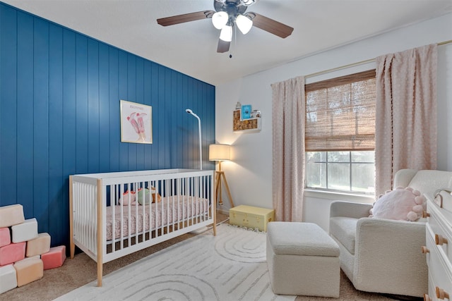 carpeted bedroom with a crib and a ceiling fan