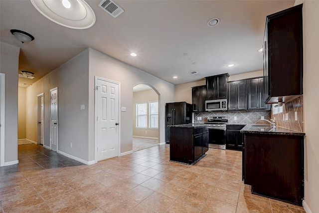 kitchen featuring a center island, arched walkways, stainless steel appliances, tasteful backsplash, and visible vents