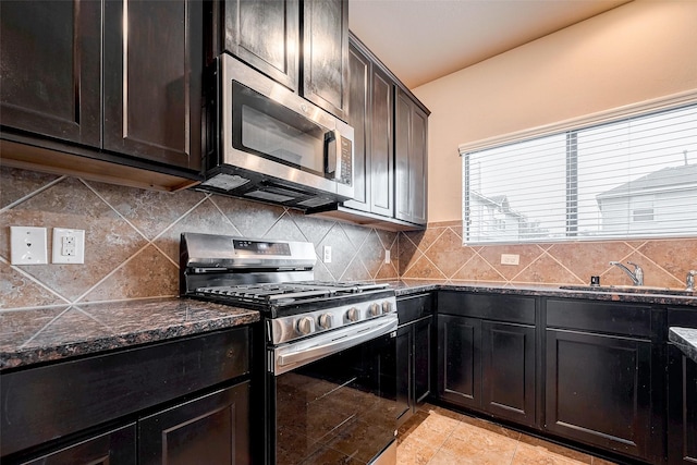 kitchen featuring appliances with stainless steel finishes, backsplash, dark stone countertops, and a sink