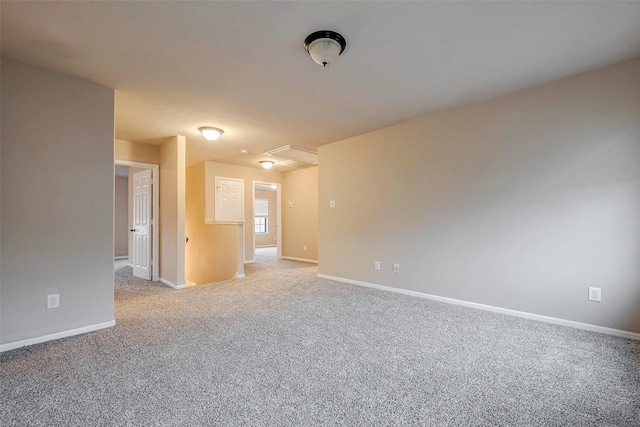 spare room featuring attic access, light carpet, and baseboards