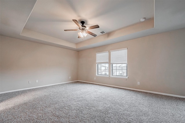 carpeted empty room with baseboards, a tray ceiling, and a ceiling fan