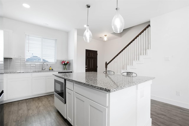 kitchen featuring a sink, tasteful backsplash, wood finished floors, and light stone countertops