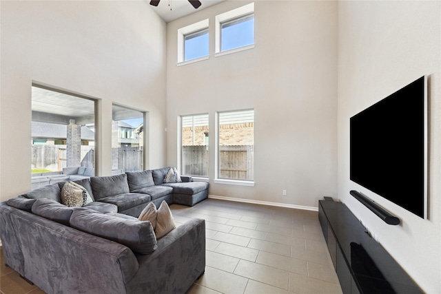 living area with a ceiling fan, a towering ceiling, baseboards, and tile patterned floors