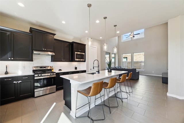 kitchen featuring appliances with stainless steel finishes, a sink, under cabinet range hood, a kitchen bar, and backsplash