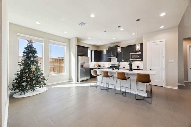 kitchen featuring a breakfast bar area, stainless steel appliances, visible vents, light countertops, and an island with sink