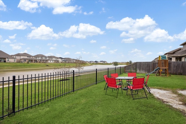 view of yard featuring a residential view, a playground, fence, and a water view