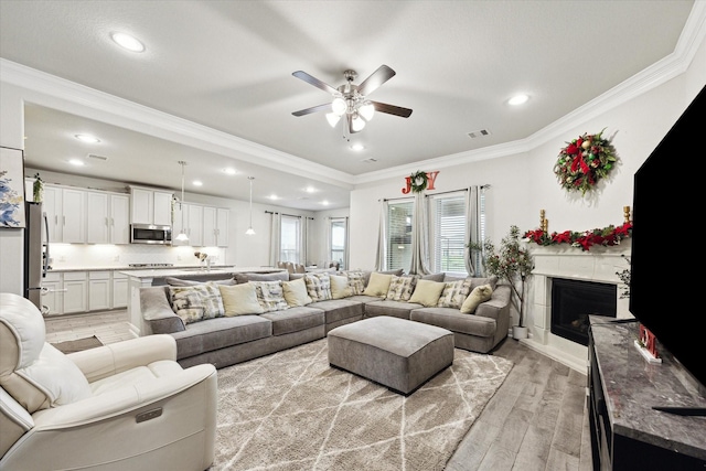 living area with crown molding, a fireplace, recessed lighting, visible vents, and light wood-style floors