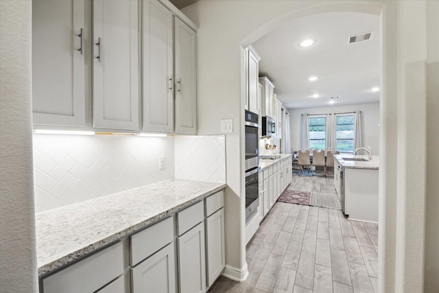 kitchen with arched walkways, stainless steel appliances, visible vents, backsplash, and wood tiled floor