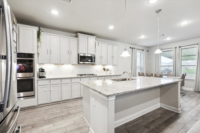 kitchen with tasteful backsplash, a center island with sink, wood tiled floor, stainless steel appliances, and a sink