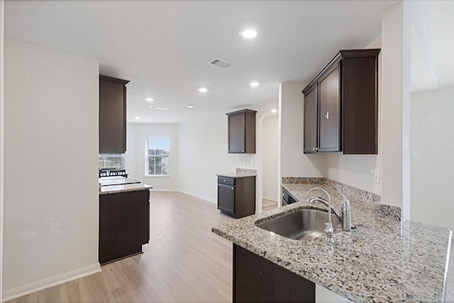 kitchen with light stone counters, light wood-style flooring, a sink, and dark brown cabinetry